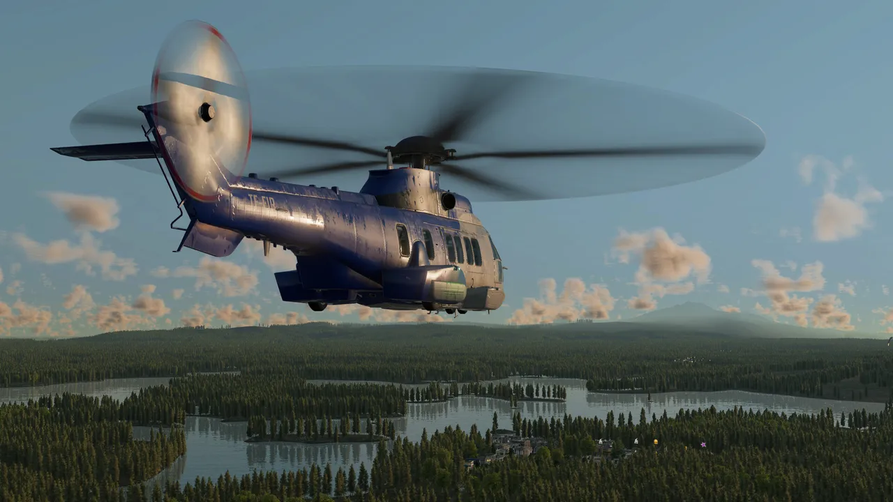 A dark blue helicopter flying low over a wide landscape of forest and lakes