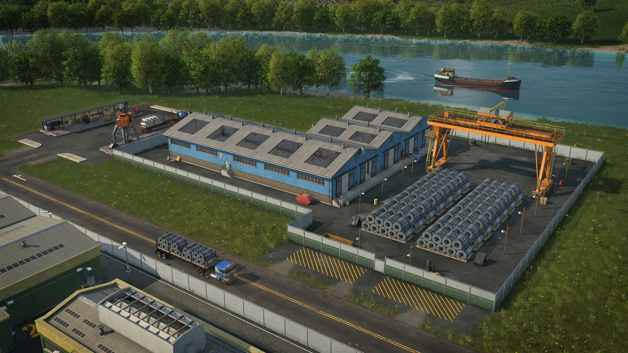 An industrial yard on a riverbank with a large shed, a yellow gantry crane and stacked pipes, a ship on the river